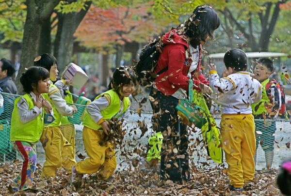 가을소풍을 나온 어린이들이 낙엽을 던지며 즐거운 시간을 갖고 있다.